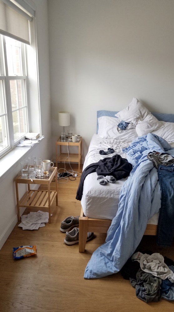Bedroom before cleaning, unmade bed and clothes piled up